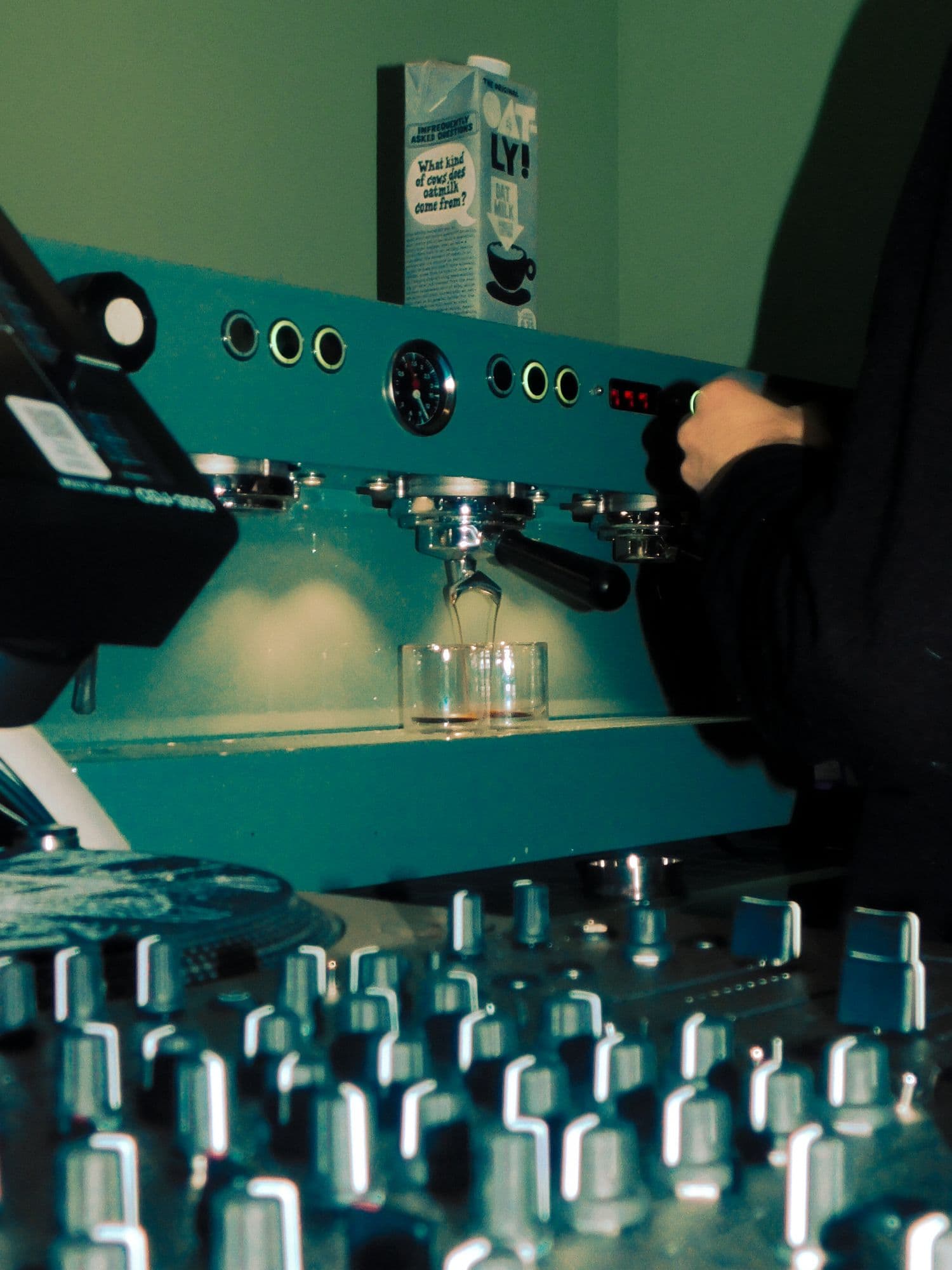 Teal-green photos of an espresso shot pulling behind a DJ mixer's knobs, and two DJs playing vinyl at a tiled bar beside the espresso machine.